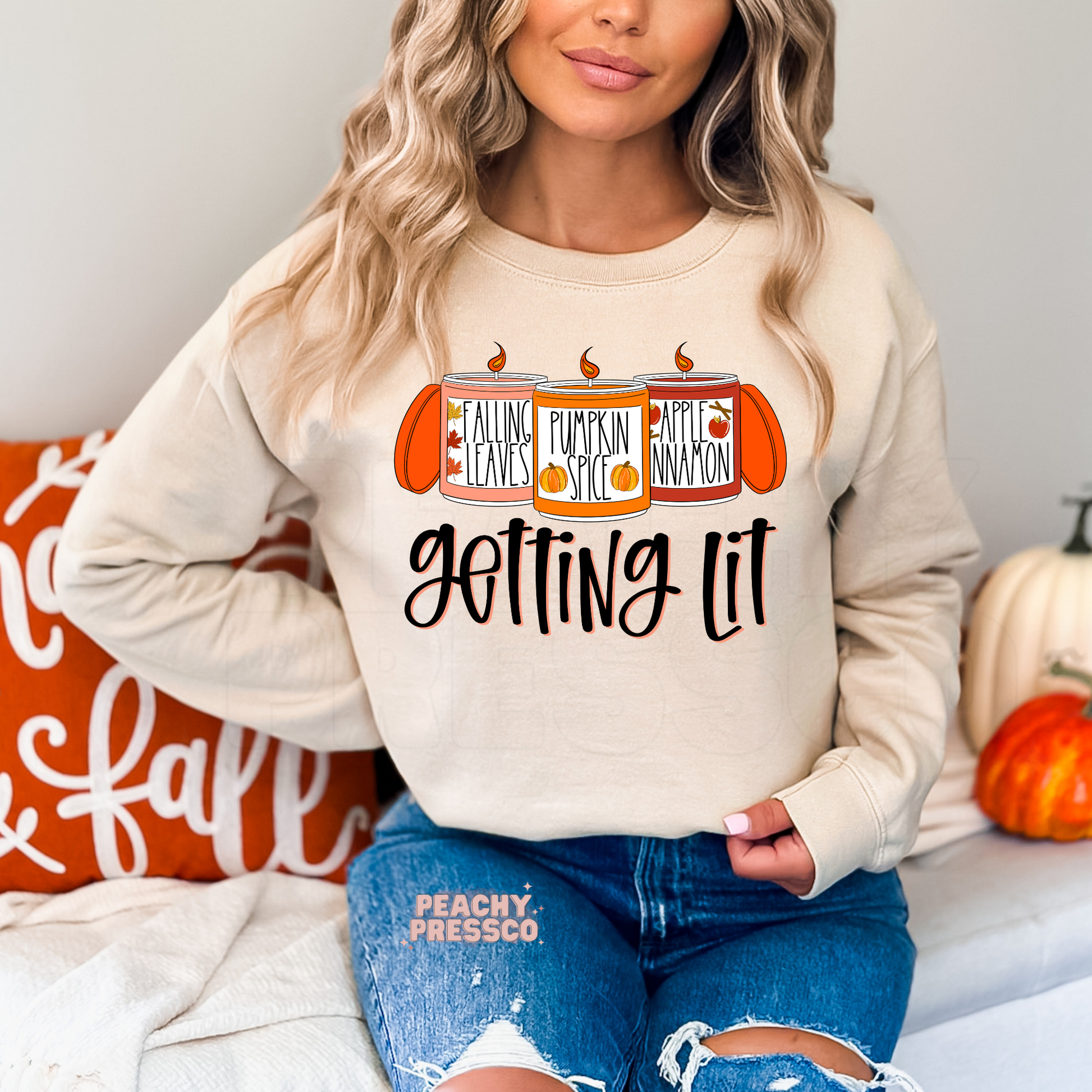 Woman wearing a sand crewneck sweatshirt with a cute "Getting Lit" autumn candle graphic featuring pumpkin spice, falling leaves, and apple cinnamon scents.