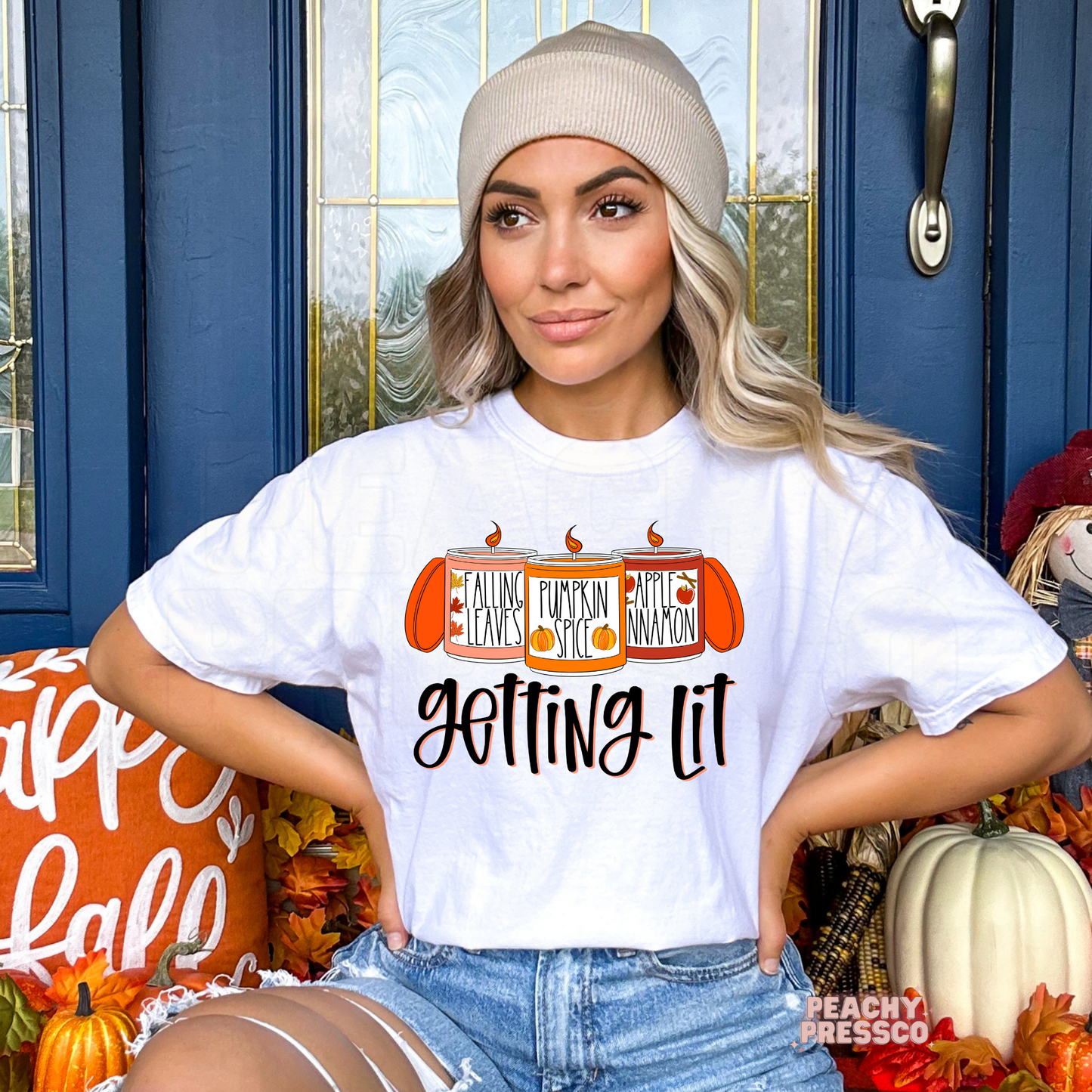 Woman wearing a white t-shirt featuring a funny "Getting Lit" fall graphic with pumpkin spice, falling leaves, and apple cinnamon candles for autumn.