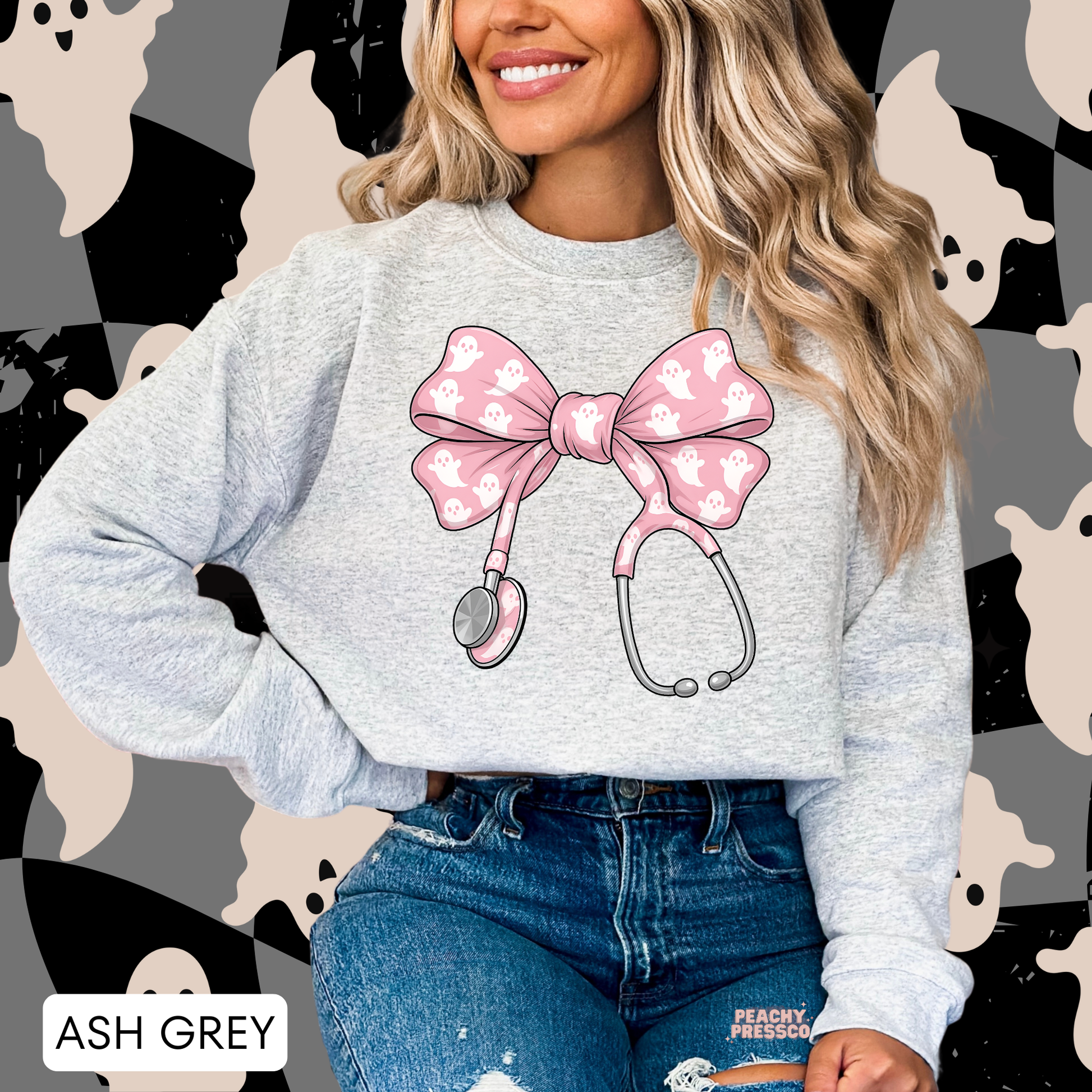 Woman wearing an ash grey crewneck sweatshirt featuring a pink ghost stethoscope bow design for Halloween nurses and healthcare professionals.