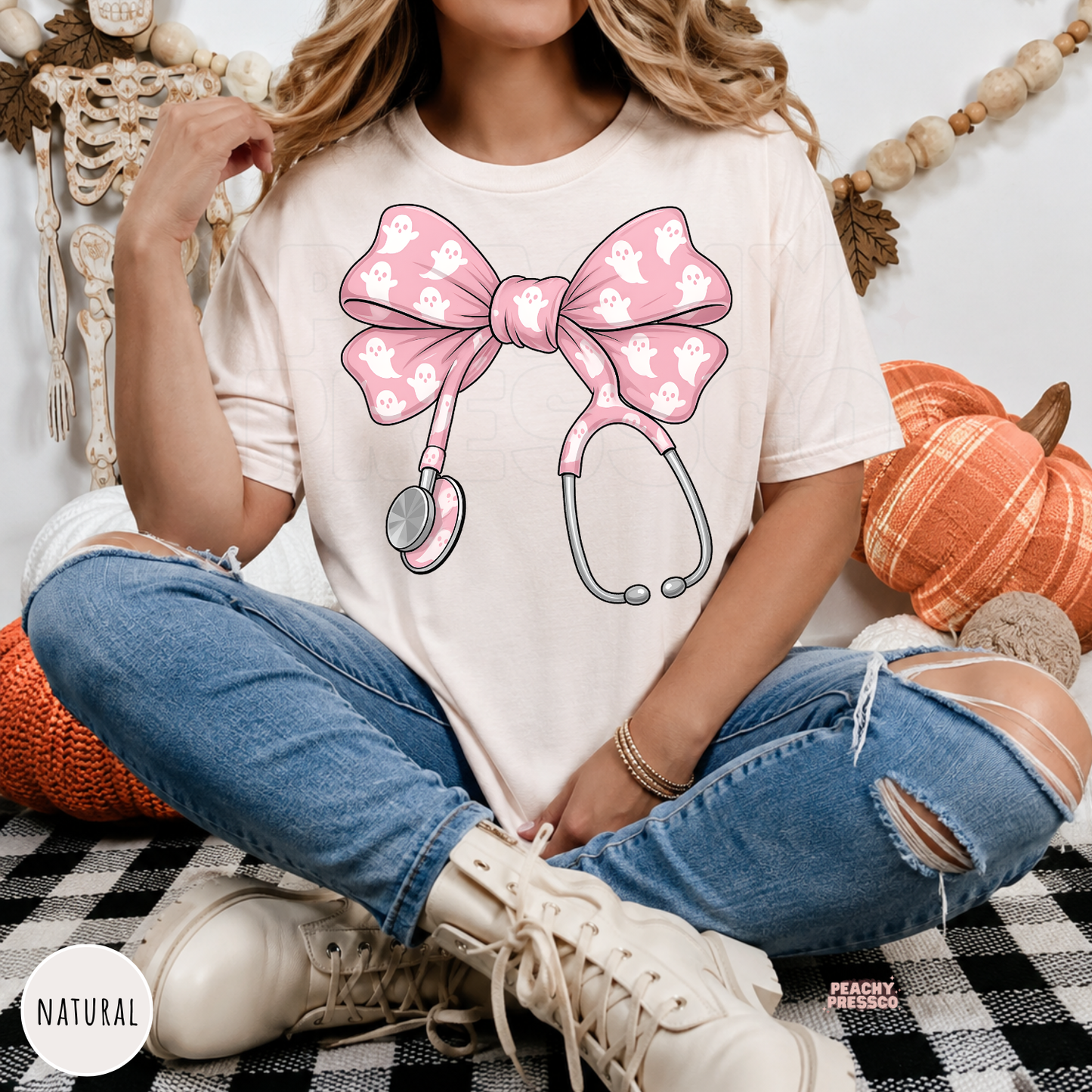 Woman wearing a natural Halloween nurse t-shirt with a pink ghost stethoscope bow design in a cute coquette aesthetic.