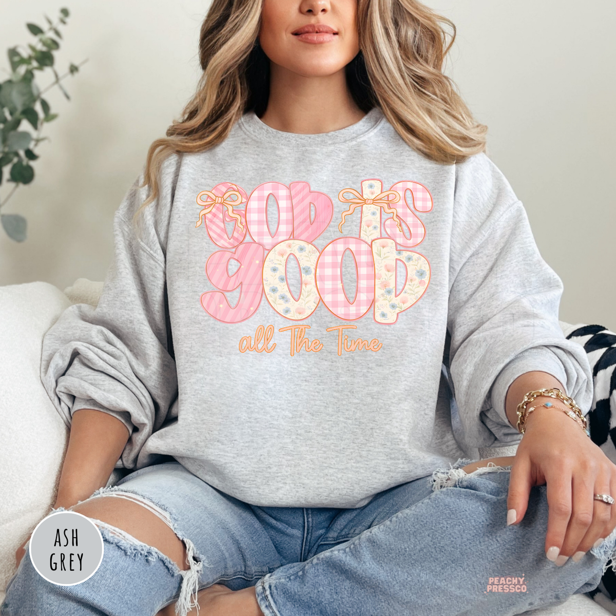 Ash Grey Gildan crewneck sweatshirt featuring a pastel "God Is Good All The Time" graphic with floral and gingham lettering, soft pink bows, and a feminine Christian faith design.