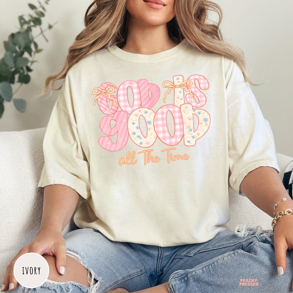 Ivory Comfort Colors garment-dyed t-shirt featuring a pastel "God Is Good All The Time" design with pink gingham letters, floral patterns, and dainty bows. Relaxed unisex Christian graphic tee perfect for everyday faith-inspired style.