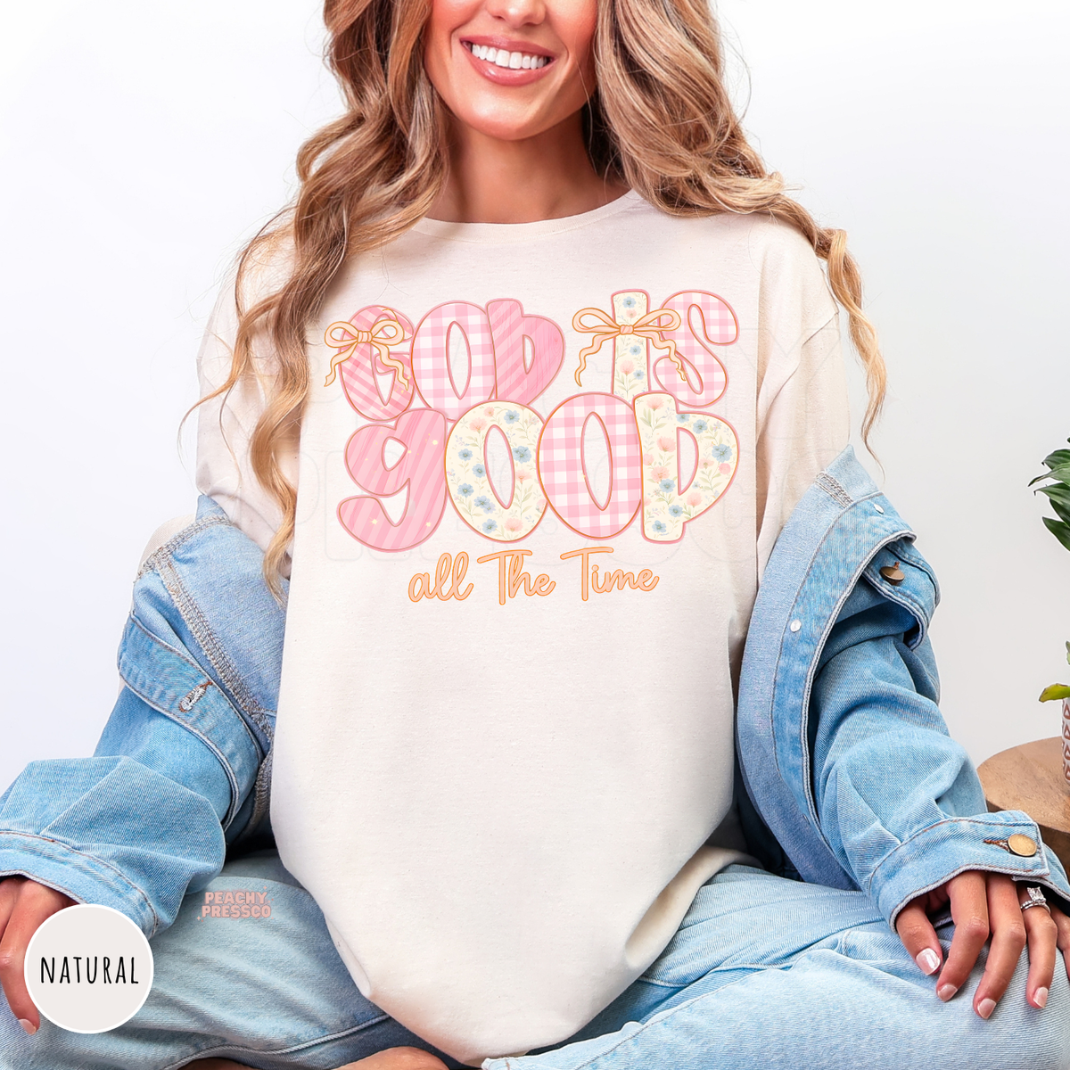Natural color t-shirt featuring a pastel "God Is Good All The Time" graphic with pink gingham, floral lettering, and delicate bow accents. Soft unisex Christian faith tee with a feminine cottagecore aesthetic.