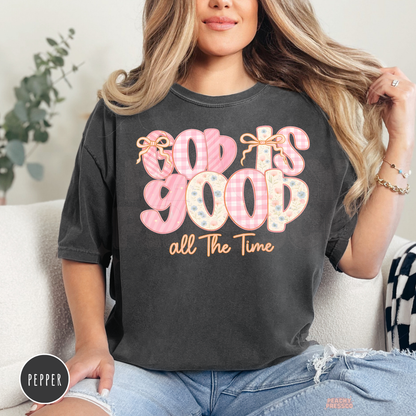 Pepper Comfort Colors garment-dyed t-shirt featuring a pastel "God Is Good All The Time" graphic with floral and gingham lettering and bow details. Vintage-inspired unisex Christian faith tee with a soft feminine design.