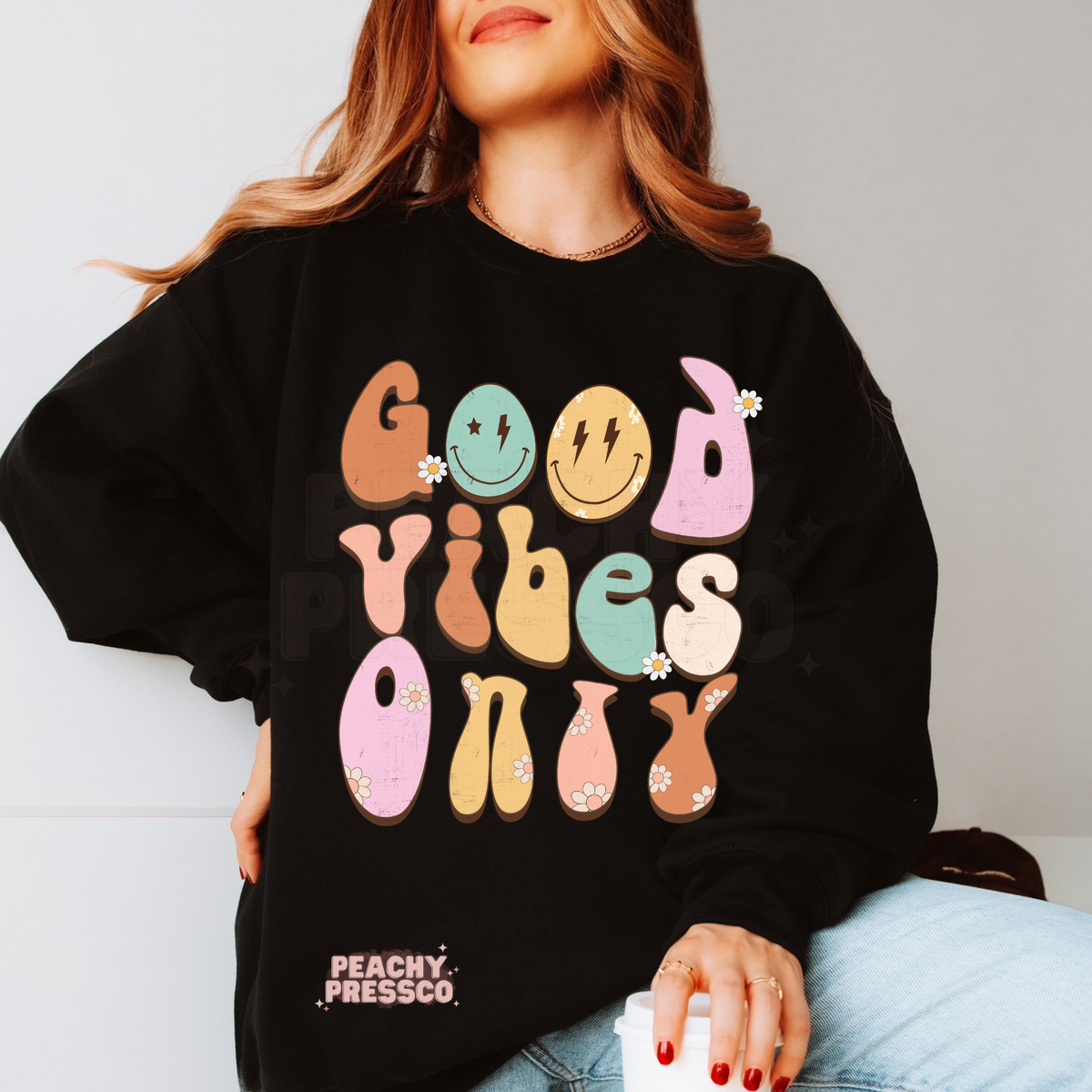 Black sweatshirt featuring a colorful "Good Vibes Only" retro graphic with pastel groovy lettering, smiley faces, daisy flowers, and a fun vintage look.