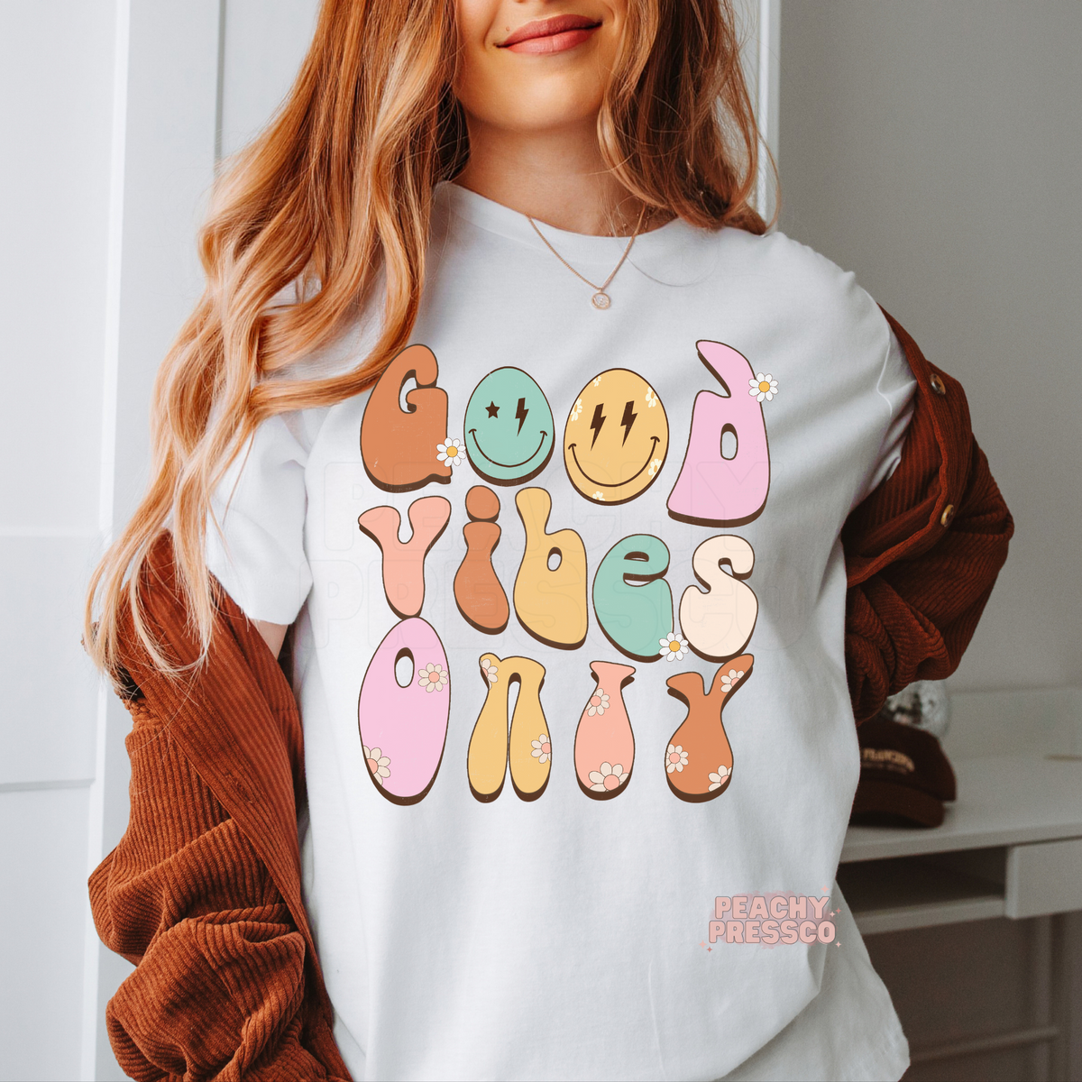 White t-shirt with a retro "Good Vibes Only" graphic featuring pastel bubble lettering, smiley faces, daisy accents, and a cheerful vintage aesthetic.