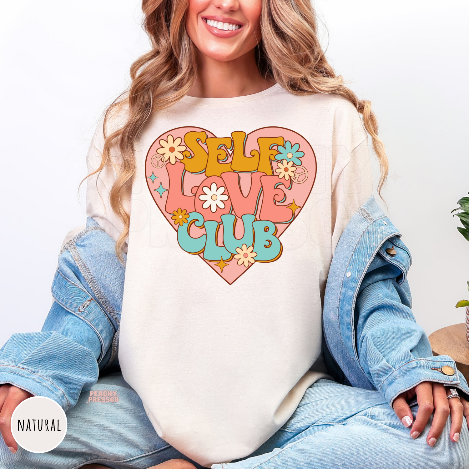 Natural t-shirt displaying a vintage Self Love Club heart design with retro typography, pastel flowers, and boho-inspired accents.