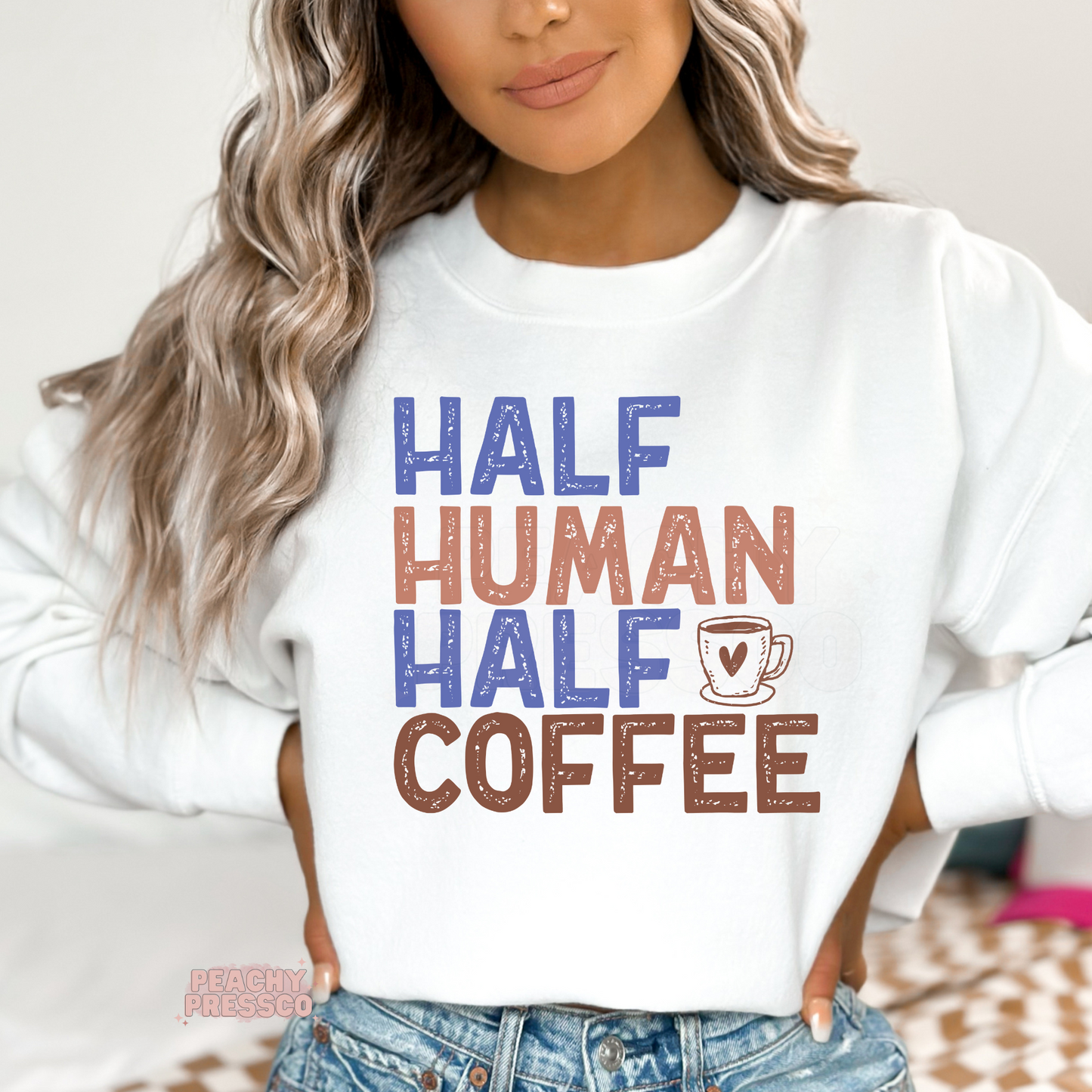 Woman wearing a white graphic sweatshirt featuring the funny "Half Human Half Coffee" design with a coffee cup illustration in vintage distressed lettering.