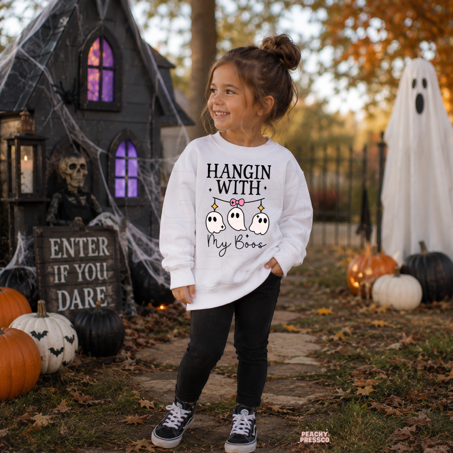 Girl wearing a white Hangin With My Boos Halloween sweatshirt featuring three cute hanging ghosts with a pink bow.