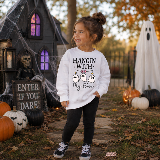 Girl wearing a white Hangin With My Boos Halloween sweatshirt featuring three cute hanging ghosts with a pink bow.