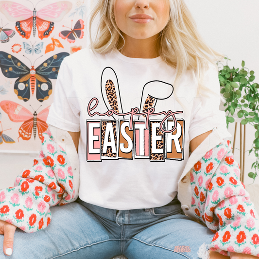 White t-shirt featuring a Happy Easter graphic with leopard print bunny ears and pink spring lettering.
