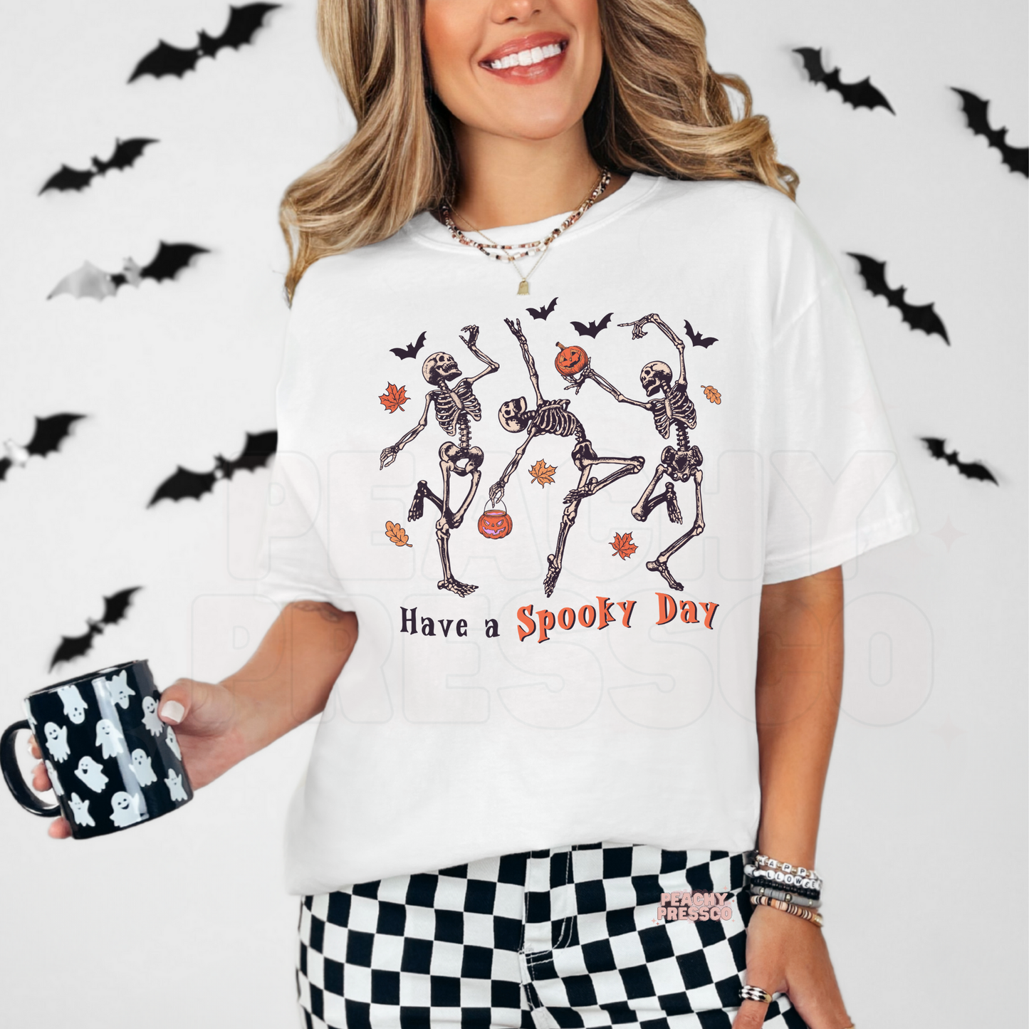 Woman wearing a white Halloween t-shirt featuring dancing skeletons, pumpkins and the phrase "Have a Spooky Day."