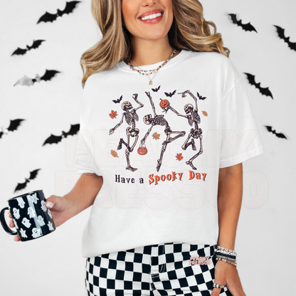 Woman wearing a white Halloween t-shirt featuring dancing skeletons, pumpkins and the phrase "Have a Spooky Day."