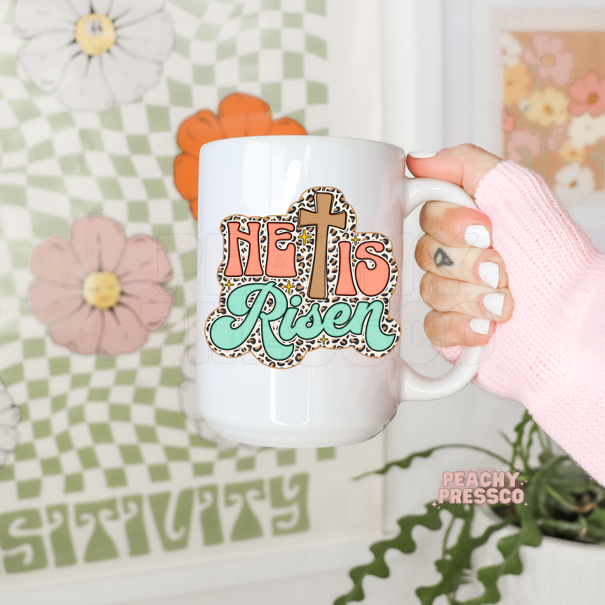 White ceramic coffee mug featuring a retro "He Is Risen" Christian design with a brown cross, coral lettering, mint script, leopard print outline, and sparkling accents. Faith-inspired Easter gift mug.