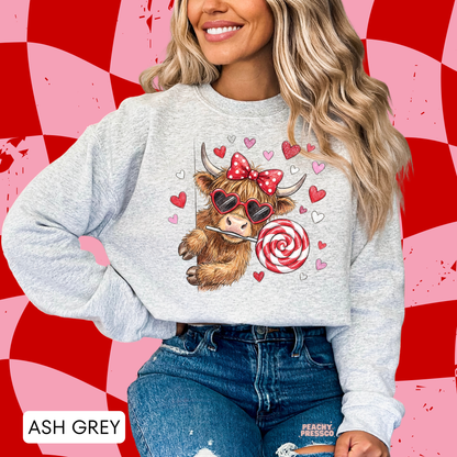 Ash grey sweatshirt with a whimsical Valentine's cow graphic featuring oversized heart sunglasses, a swirl lollipop, and pink and red hearts.
