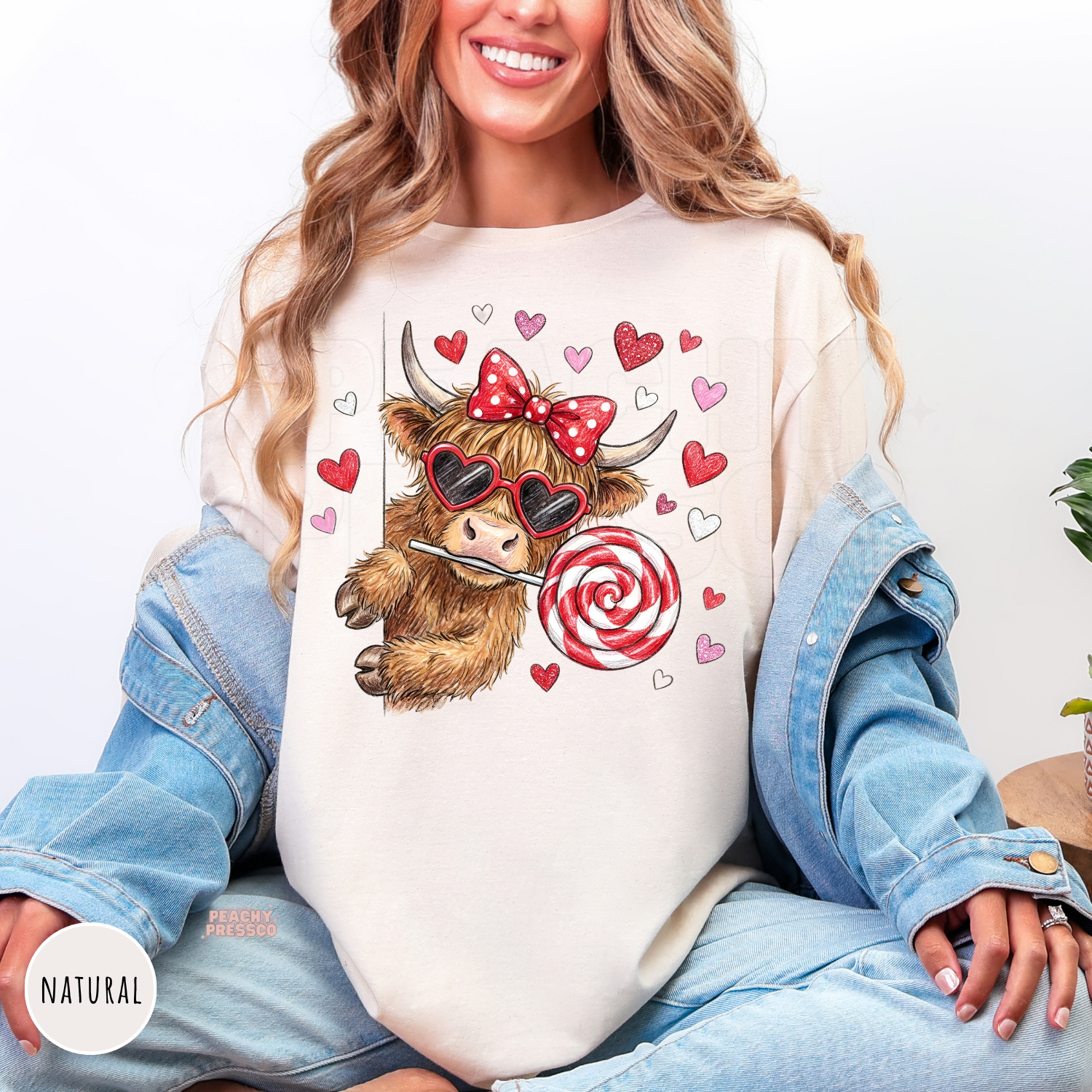 Natural graphic tee featuring an adorable cow with heart sunglasses, a candy lollipop, pink bow, and floating Valentine's hearts.