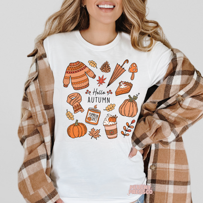 Woman wearing a white t-shirt layered with a plaid flannel featuring a Hello Autumn graphic with pumpkins, pumpkin spice latte, sweater, scarf, mushrooms, pie, and cozy fall elements.