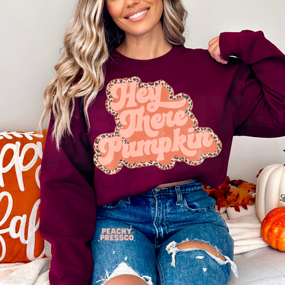 Woman wearing a maroon crewneck sweatshirt featuring a retro Hey There Pumpkin design with a leopard print outline, perfect for Thanksgiving and fall.