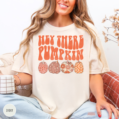 Woman wearing an ivory Comfort Colors t-shirt featuring a retro "Hey There Pumpkin" design with colorful patterned pumpkins for fall.