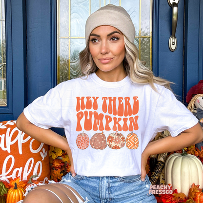 Woman wearing a white t-shirt with a retro "Hey There Pumpkin" fall graphic featuring decorative pumpkins in warm seasonal colors.