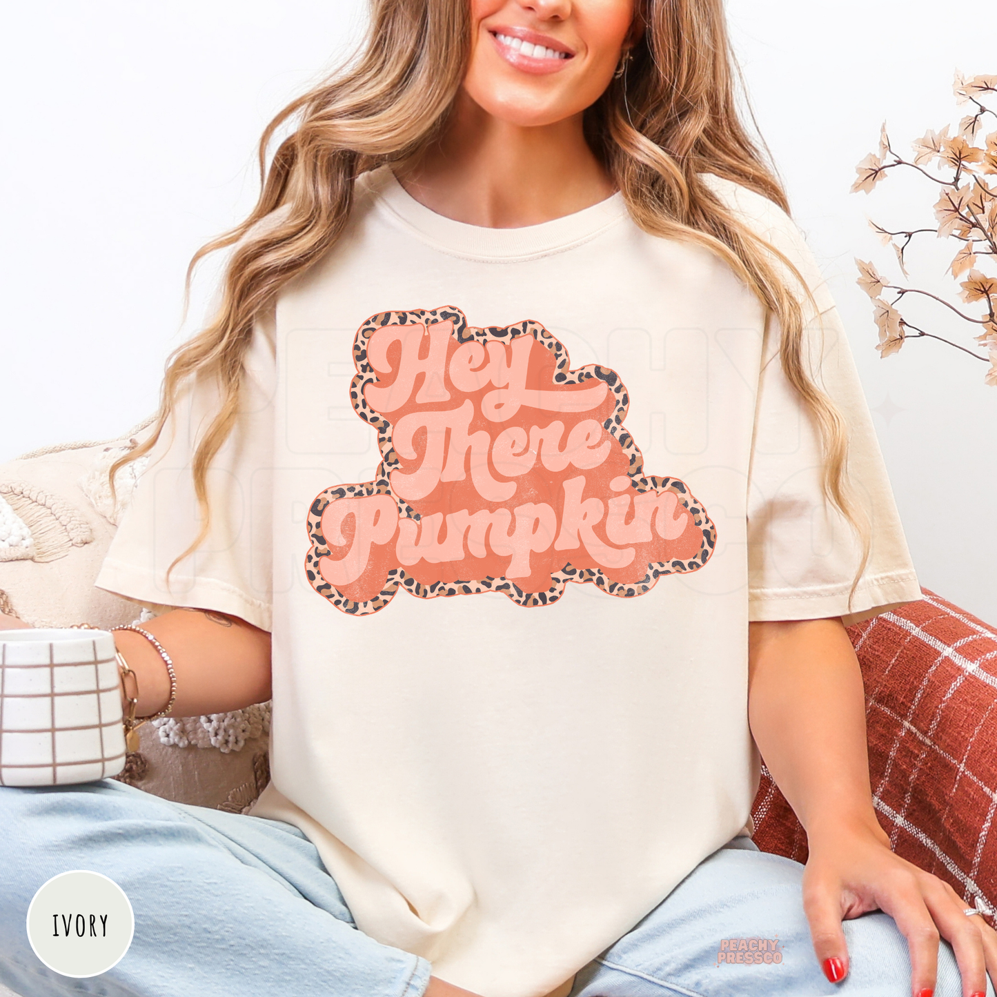 Woman wearing an ivory graphic t-shirt featuring a retro Hey There Pumpkin design with a leopard print border for cozy fall outfits.