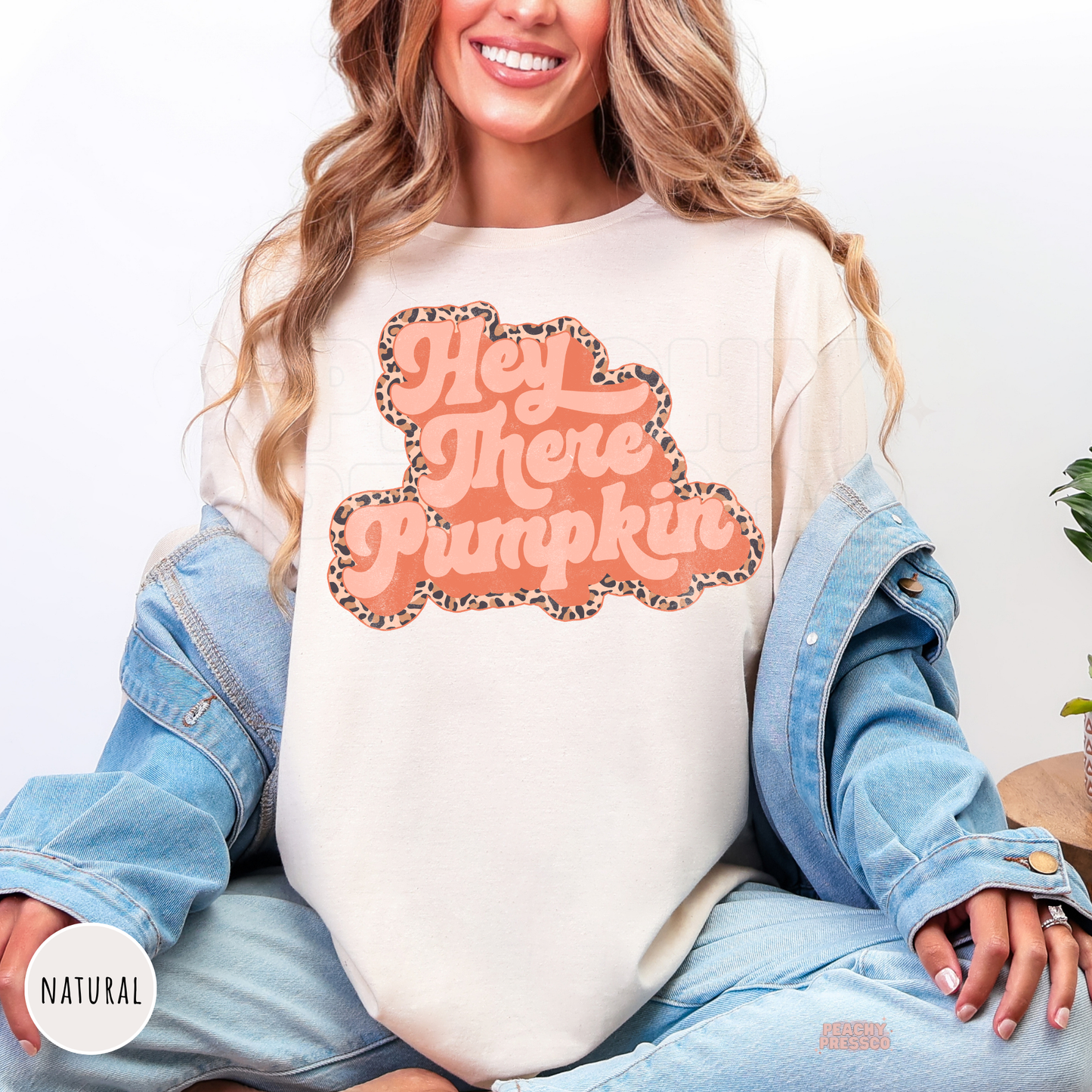 Woman wearing a natural graphic t-shirt featuring a retro Hey There Pumpkin design with a leopard print outline for pumpkin season.