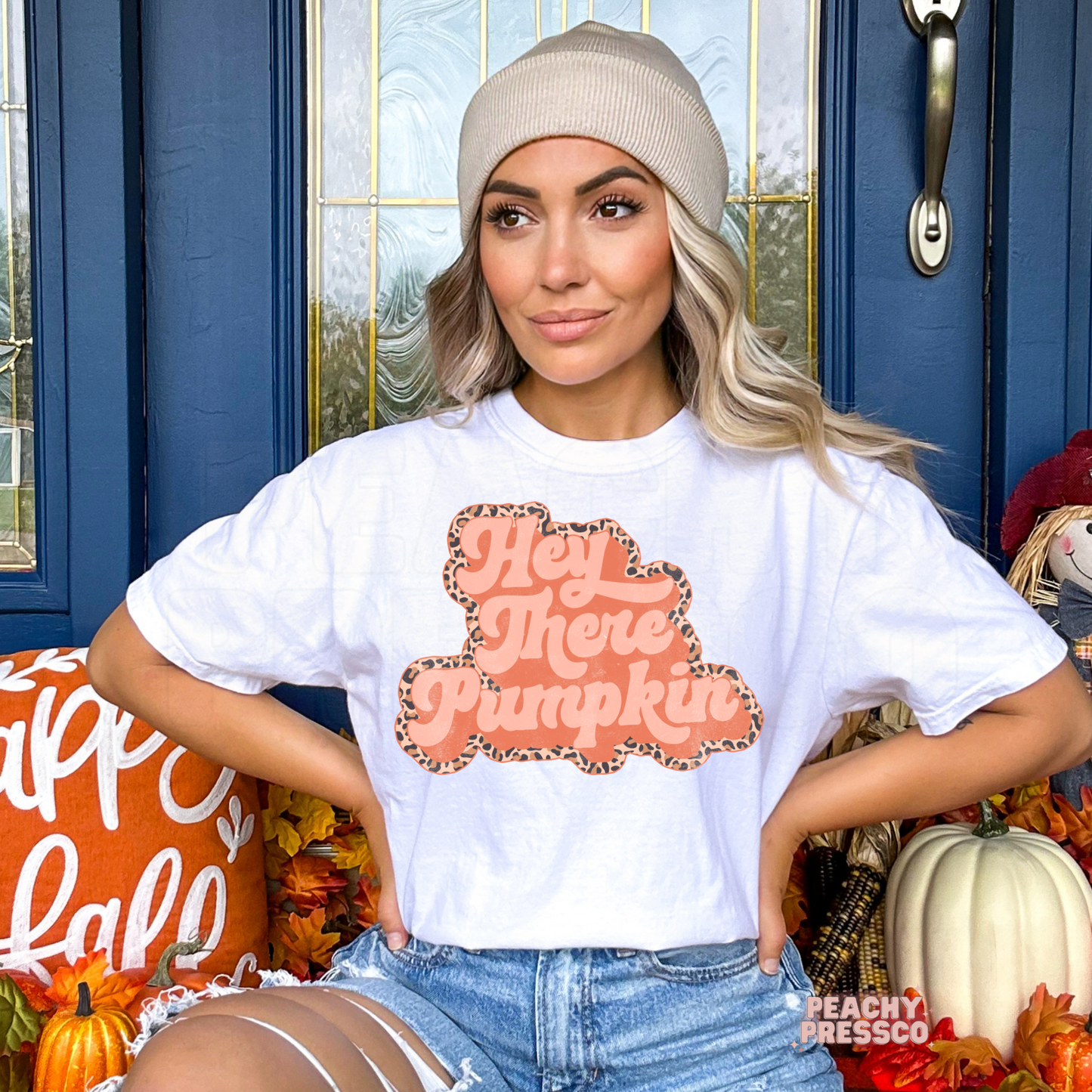 Woman wearing a white graphic t-shirt featuring a retro Hey There Pumpkin design with a leopard print outline, styled for autumn and Thanksgiving.