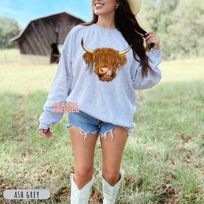 Woman wearing an ash grey sweatshirt with a realistic Highland cow graphic, perfect for western fashion and country lifestyle.