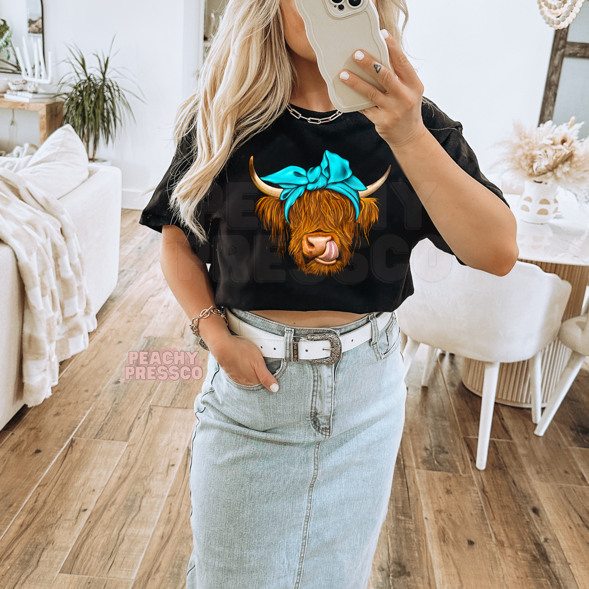 Woman wearing a black t-shirt featuring a Highland cow with a turquoise bow graphic for western cowgirl style.