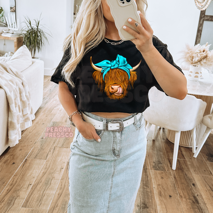 Woman wearing a black t-shirt featuring a Highland cow with a turquoise bow graphic for western cowgirl style.
