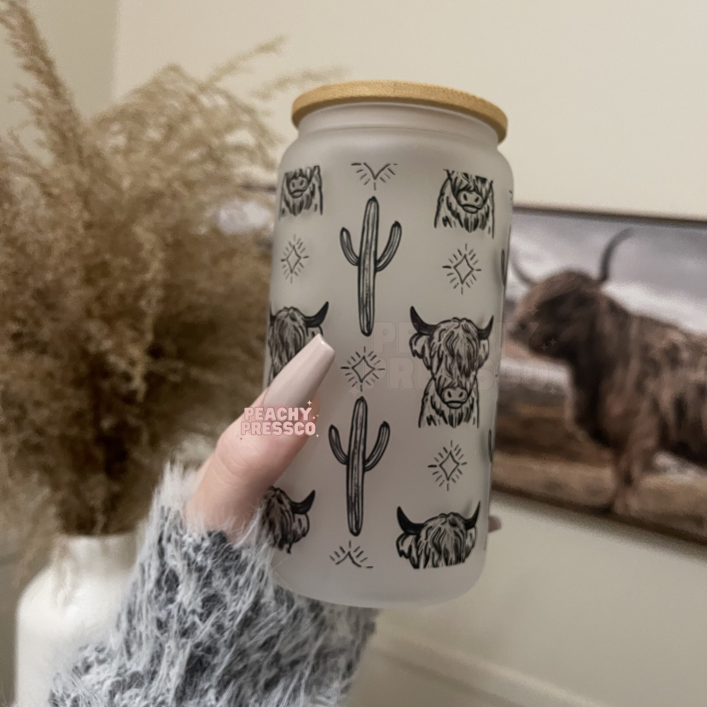Frosted glass can featuring repeating Highland cow illustrations, cacti, and western-inspired accents with bamboo lid and straw.