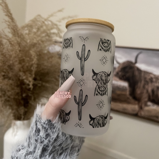 Frosted glass can featuring repeating Highland cow illustrations, cacti, and western-inspired accents with bamboo lid and straw.