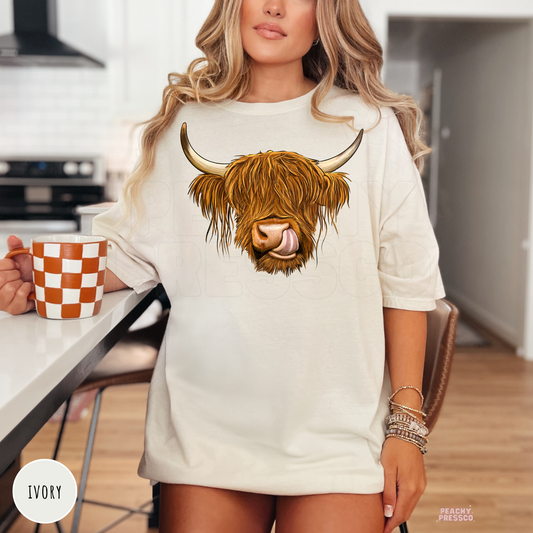 Woman wearing an ivory graphic t-shirt with a Highland cow illustration, ideal for western, ranch, and farmhouse lovers.