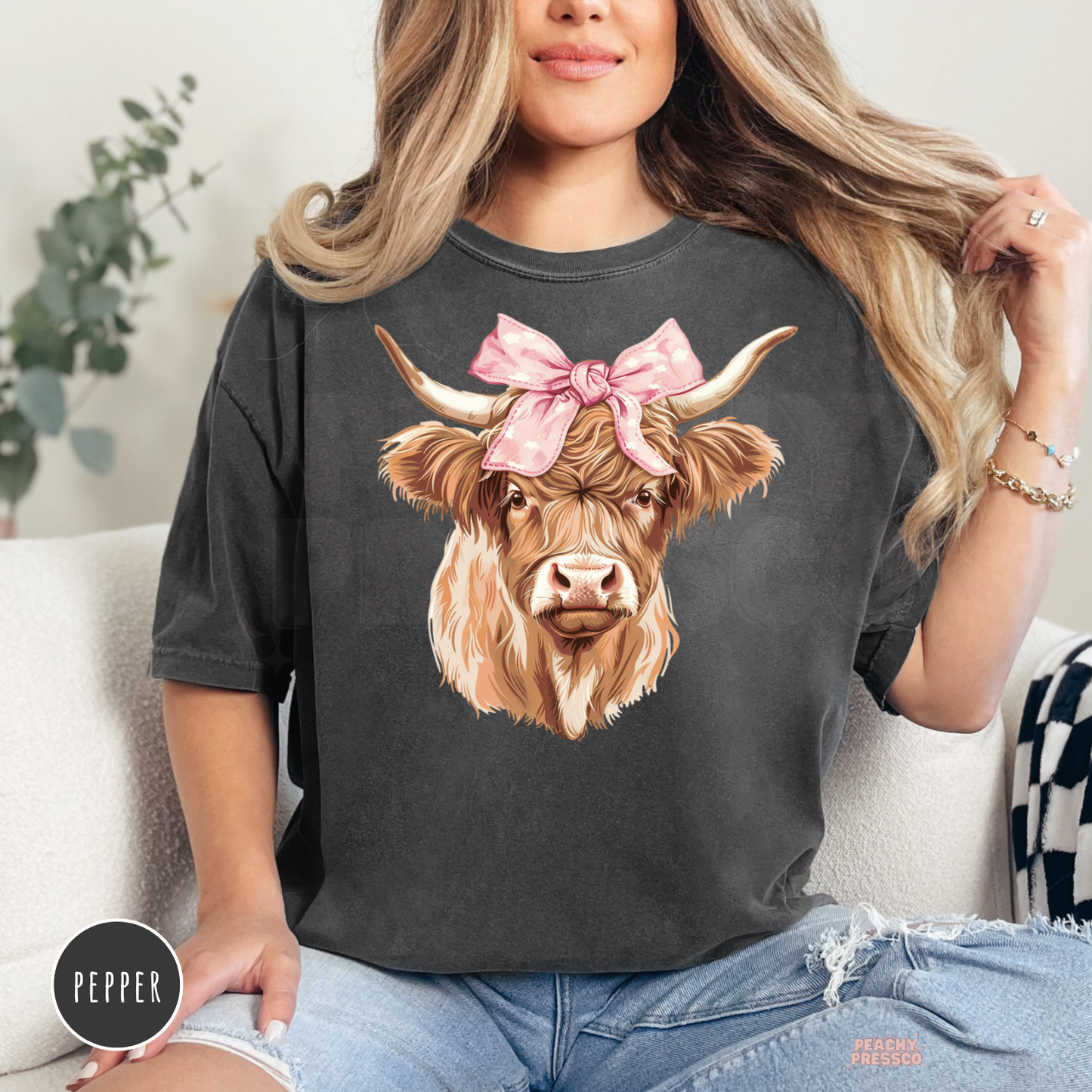 Woman wearing a pepper Comfort Colors t-shirt featuring a Highland cow with a pink bow in a western country graphic design.
