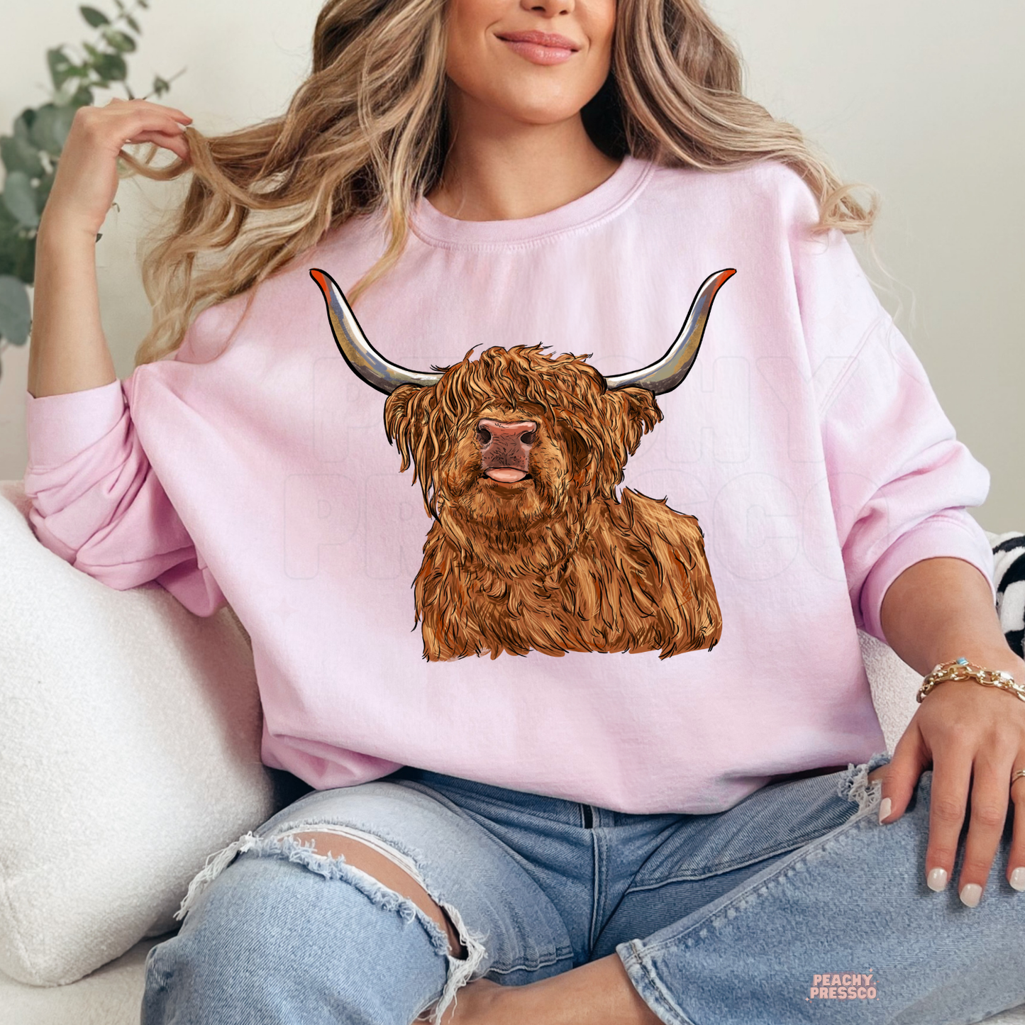 Woman wearing a light pink sweatshirt with a realistic Highland cow graphic, ideal for country living and western fashion.