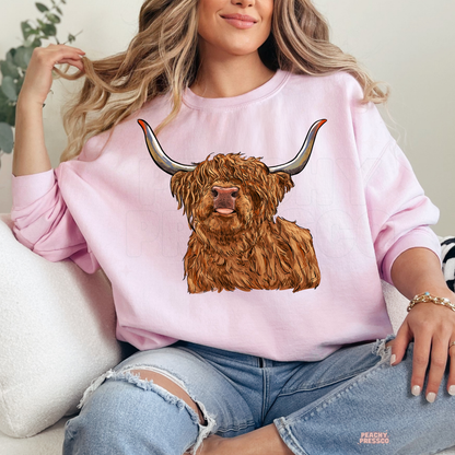 Woman wearing a light pink sweatshirt with a realistic Highland cow graphic, ideal for country living and western fashion.