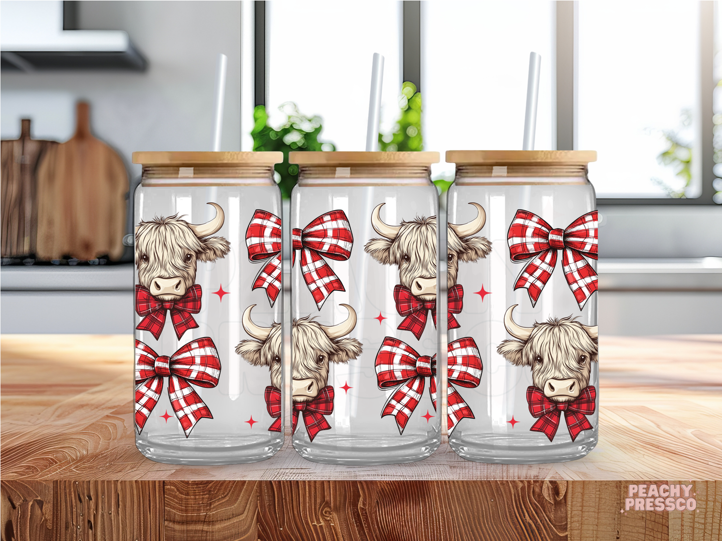 Glass cup with highland cow design and red bows on a wooden surface.