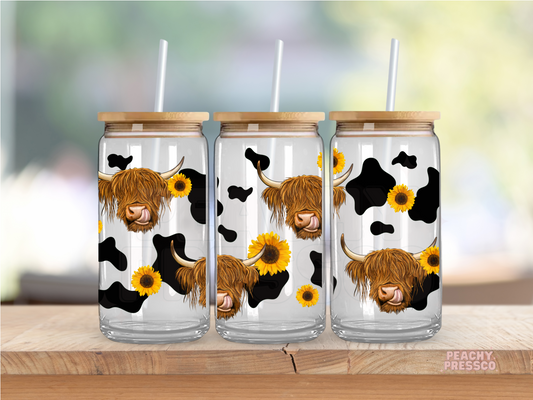 Glass cup featuring repeating Highland cow faces with sunflower accents and black cow print pattern.
