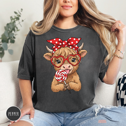 Pepper Comfort Colors t-shirt featuring a cute Highland cow with heart-shaped glasses, red bow, and Valentine's lollipop, perfect for farm animal lovers.