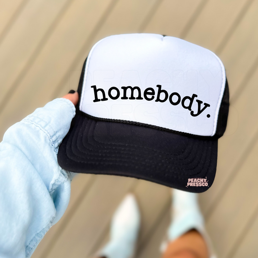 Black and white foam trucker hat with "Homebody" printed in simple black lettering. Cute minimalist hat for women who love cozy weekends, reading, relaxing at home, and everyday style.