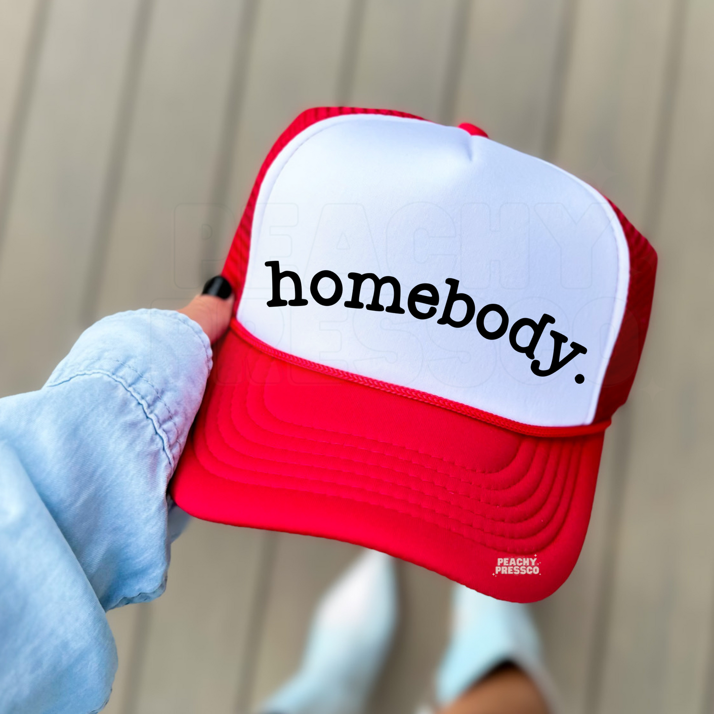 Red and white foam trucker hat featuring the word "Homebody" in minimalist black lettering. Stylish women's trucker cap for cozy lifestyles, lounging, coffee dates, travel, and casual outfits.