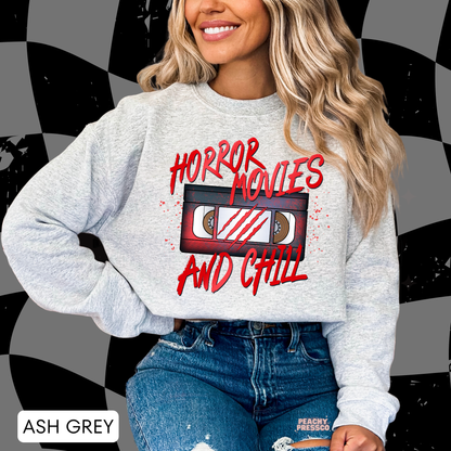 Woman wearing an ash grey crewneck sweatshirt featuring a retro VHS tape with Horror Movies and Chill graphic, perfect for Halloween movie nights.