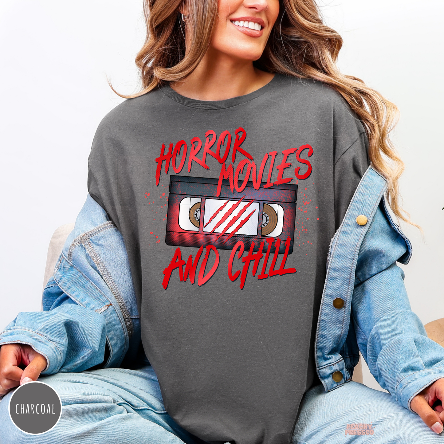 Woman wearing a charcoal crewneck sweatshirt with a Horror Movies and Chill VHS tape graphic layered under a denim jacket for fall.