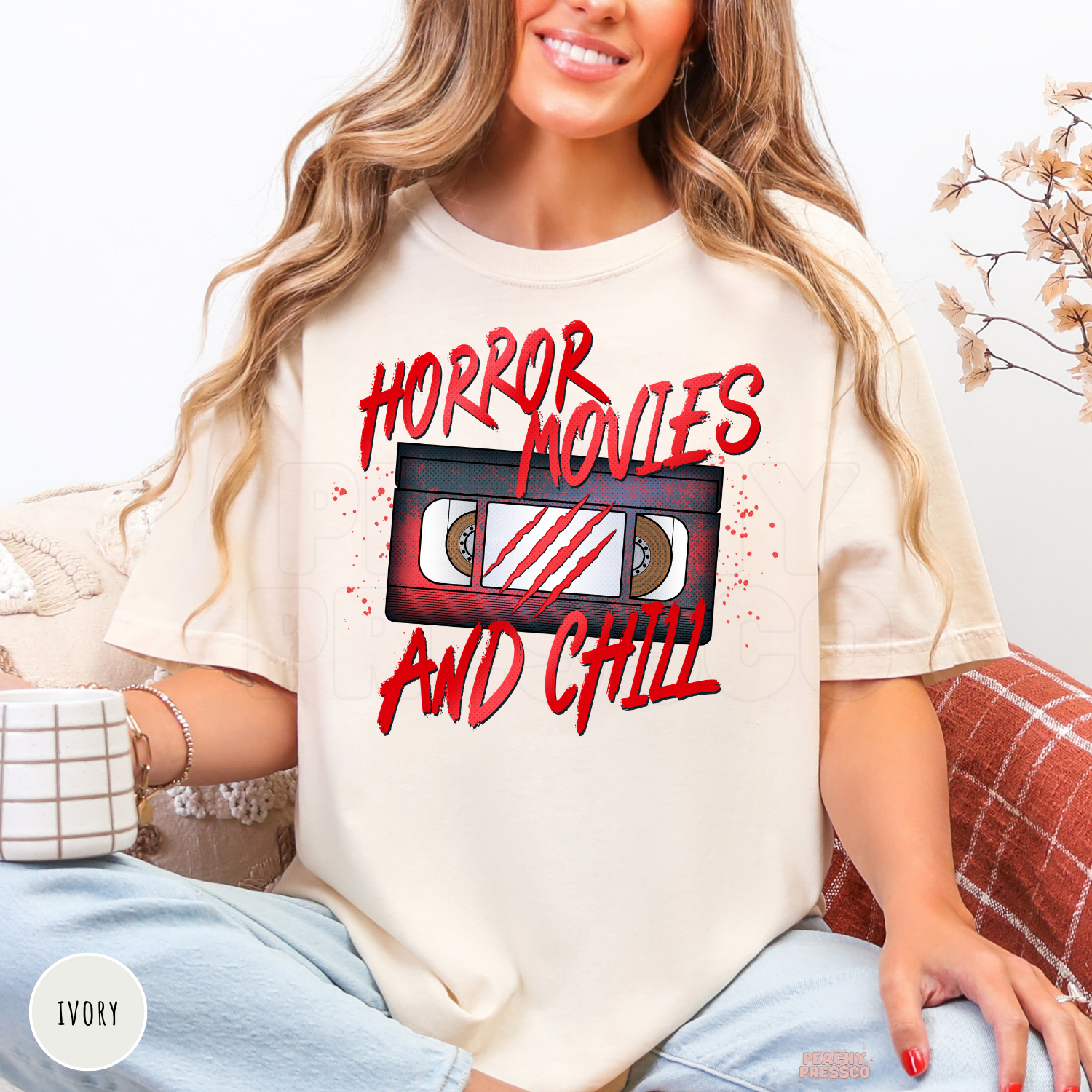 Woman wearing an ivory t-shirt featuring a Horror Movies and Chill retro VHS graphic for spooky season and Halloween.