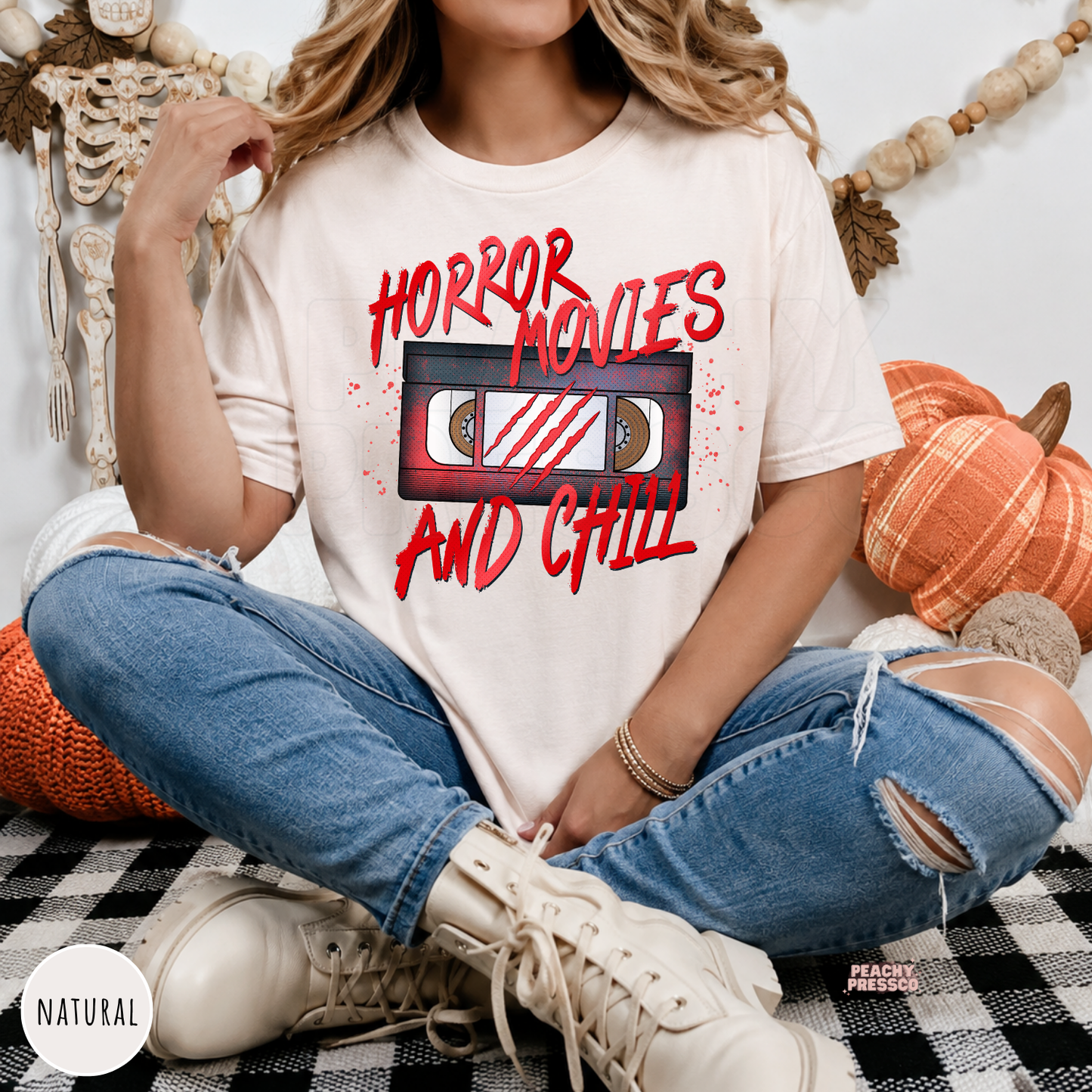 Woman wearing a natural t-shirt featuring a Horror Movies and Chill retro VHS cassette design with Halloween-inspired lettering.