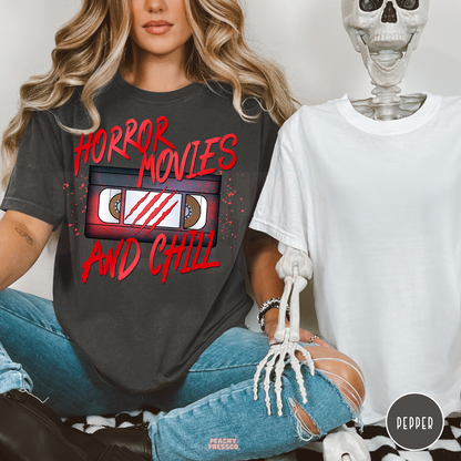 Woman wearing a pepper Comfort Colors t-shirt featuring a retro VHS tape with Horror Movies and Chill graphic, perfect for Halloween and horror movie fans.