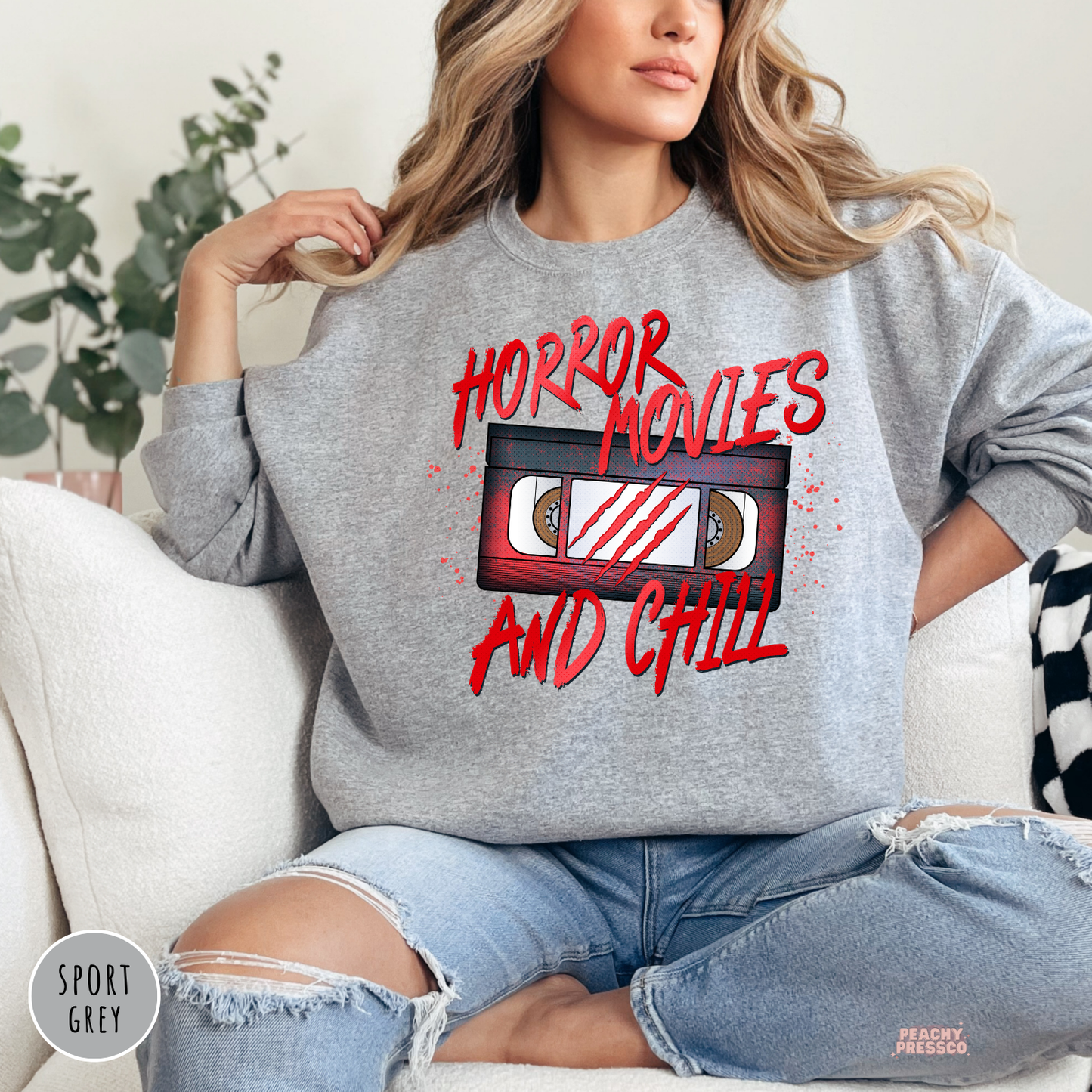 Woman wearing a sport grey sweatshirt with a Horror Movies and Chill vintage VHS tape graphic, perfect for cozy Halloween nights.