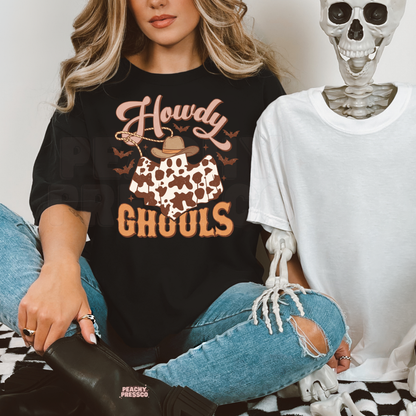 Woman wearing a black Halloween graphic t-shirt with a Howdy Ghouls cowboy ghost, cow print, bats and western spooky aesthetic.