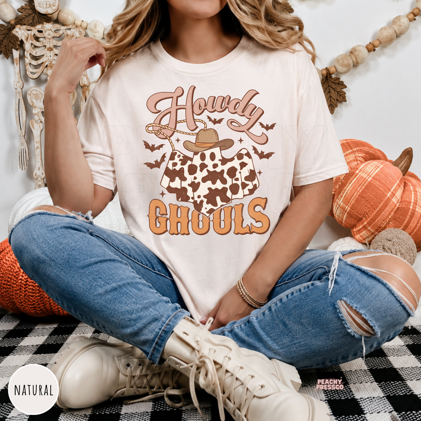 Woman wearing a natural western Halloween t-shirt featuring a cowboy ghost with cow print, bats and Howdy Ghouls retro graphic.