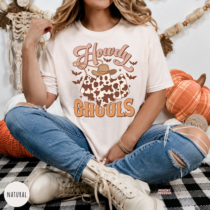 Woman wearing a natural western Halloween t-shirt featuring a cowboy ghost with cow print, bats and Howdy Ghouls retro graphic.